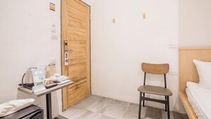 A small, clean room with a wooden door, a single bed, a chair, and a table with toiletries. - Tiintinn Inn Showtime (Taitung)