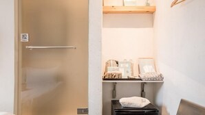 A small, compact room with a pull-down shower, a bed, a desk with a chair, and a shelf with toiletries. - Tiintinn Inn Showtime (Taitung)