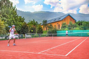 A tennis court with a net, two players, and a wooden building in the background. - Jiva Hill Resort (Crozet)