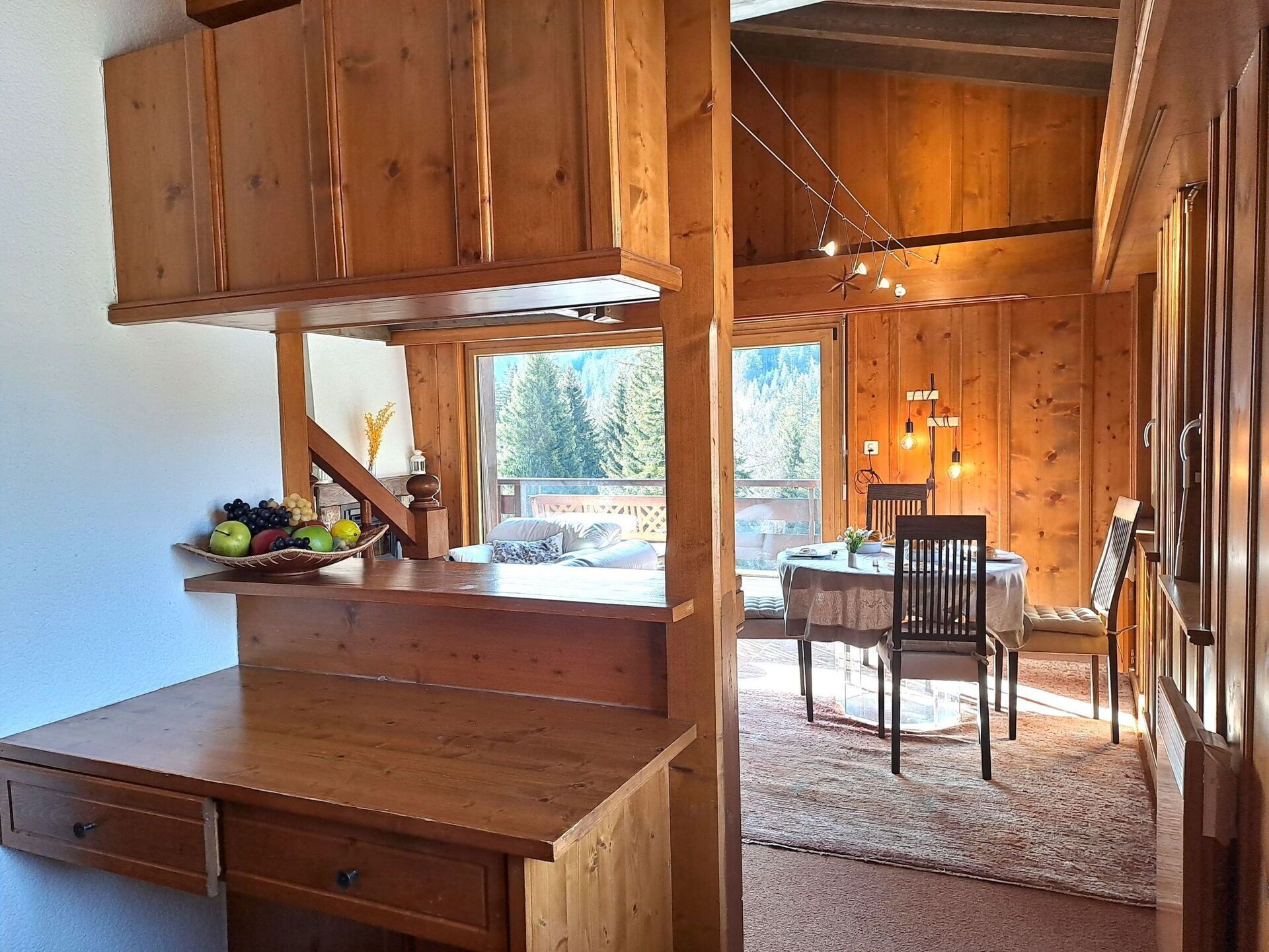 Ein Holzblockhaus-Innenraum mit Essbereich, einer Küche mit Obstschale und Blick ins Freie.