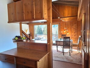 Ein Holzblockhaus-Innenraum mit Essbereich, einer Küche mit Obstschale und Blick ins Freie.