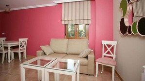 A living room with a pink wall, a beige sofa, a glass coffee table, and a white chair. - El Corcal de Liebana (Cillorigo de Liebana)