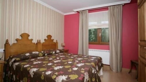A bedroom with a wooden bed, a window with curtains, and a radiator. - El Corcal de Liebana (Cillorigo de Liebana)