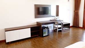 A hotel room with a desk, chair, TV, wardrobe, and a small refrigerator. - Ahaveda Resort (Phu Quoc)