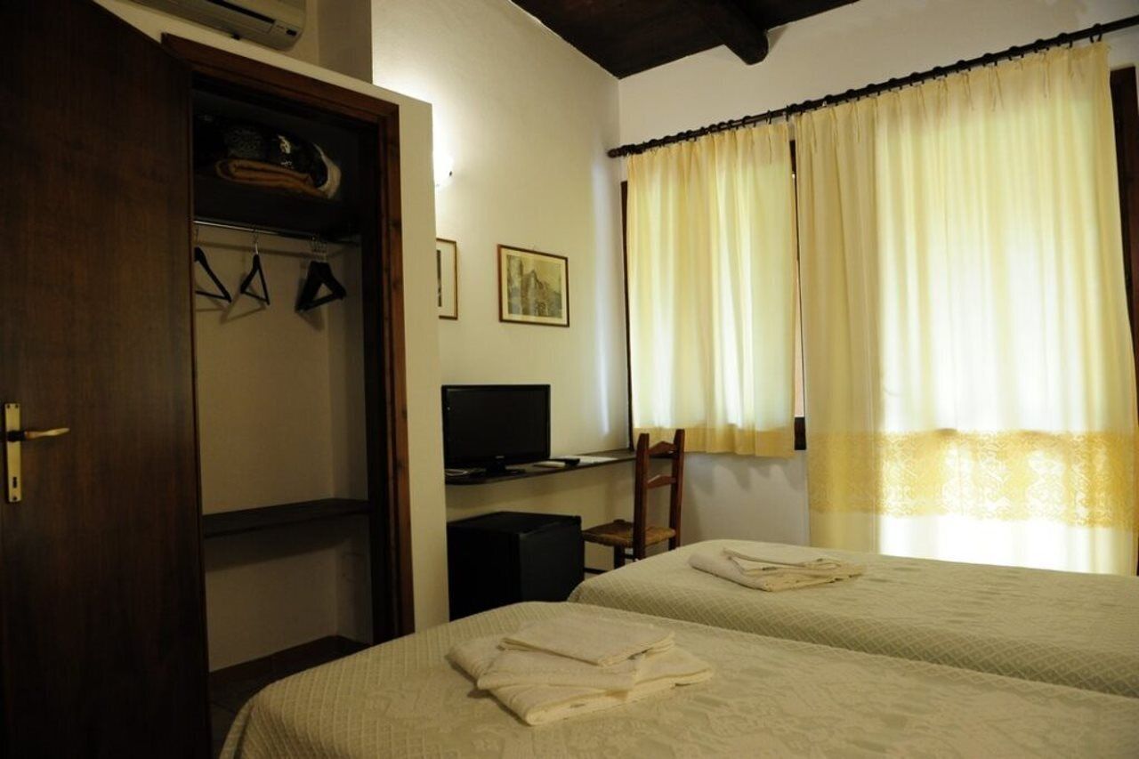 Una habitación de hotel con dos camas, televisión, armario y ventana con cortinas.