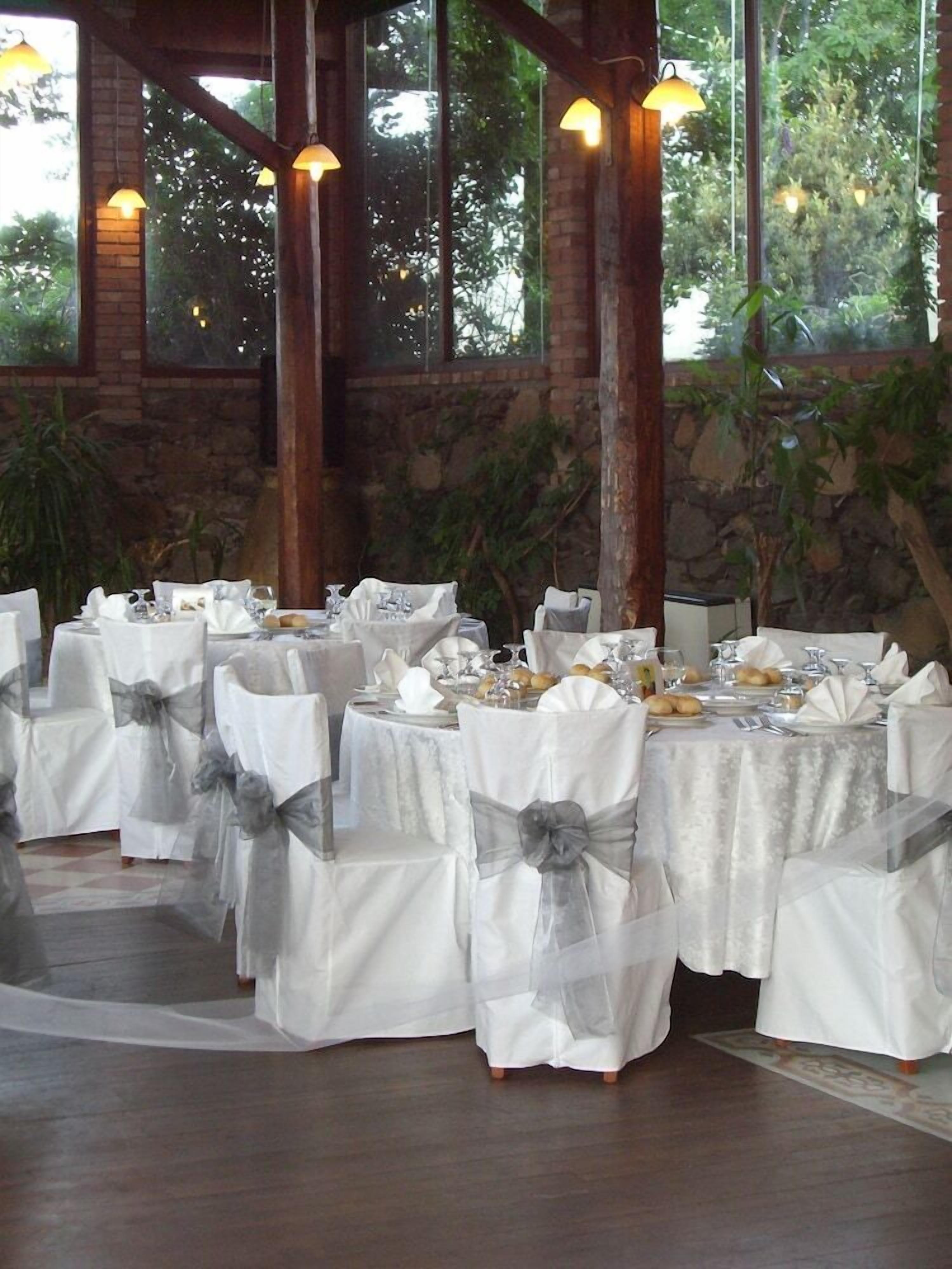 Une salle de banquet avec des tables rondes dressées pour un événement formel, agrémentée de nappes blanches et de chaises ornées de rubans gris.