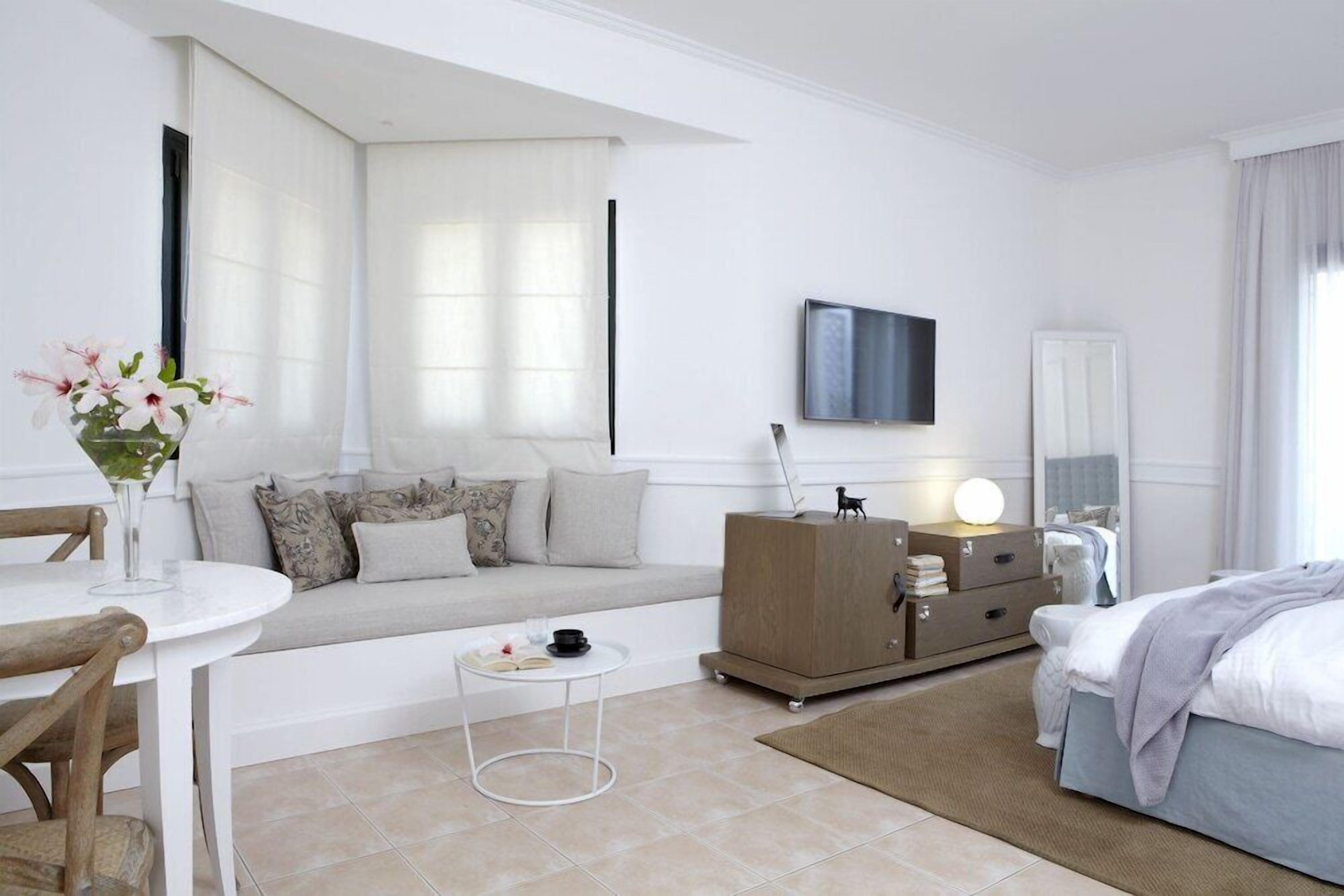 A modern hotel room with a sofa, a dining table with chairs, a TV, a dresser, and a bed.