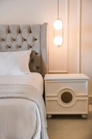 Una cama bien hecha con un cabecero capitonado, una mesita de noche con un frente redondo decorativo y una lámpara colgante.