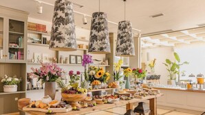 Un bufé de desayuno con arreglos florales, una estación de café y una estantería en una habitación de hotel.