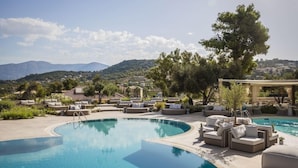 Zona de piscina con sillones de descanso y una pérgola, rodeada de vegetación y con vistas a un paisaje montañoso.