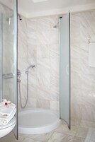 Un baño moderno con ducha de vidrio, una bañera blanca y un lavamanos con toalla y flor.