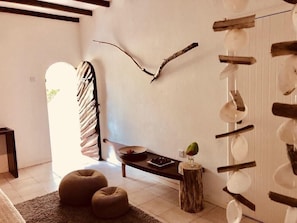 Ein modernes Wohnzimmer mit einem großen Fenster, einer Holzbank, zwei runden Hocker und einem Wandregal mit Dekorationen.