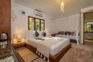 Ein Schlafzimmer mit einem Bett, Nachttischen, einer Lampe und Blick auf Grün hinter dem Fenster.