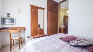 Un dormitorio con una cama, un escritorio, una silla, un televisor y un armario.