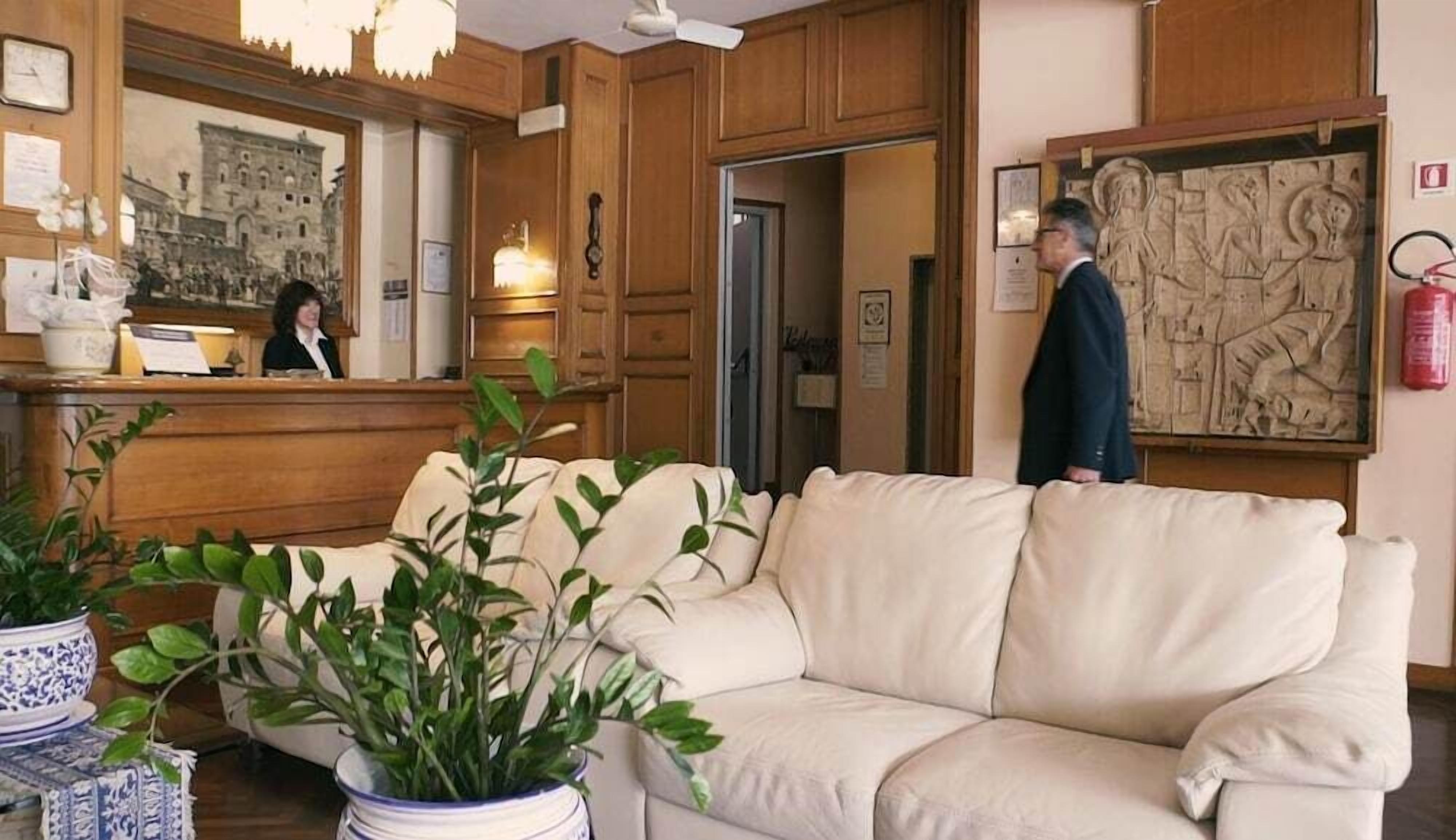 A hotel lobby with a reception desk, a beige sofa, and potted plants.