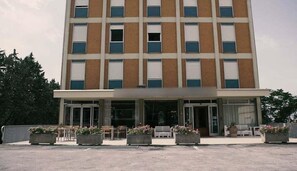 A multi-story hotel with a central entrance, outdoor seating, and a parking area. - Grifone Hotel Ristorante (Perugia)