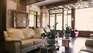 A living room with a beige sofa, a glass coffee table, and potted plants. - Grifone Hotel Ristorante (Perugia)