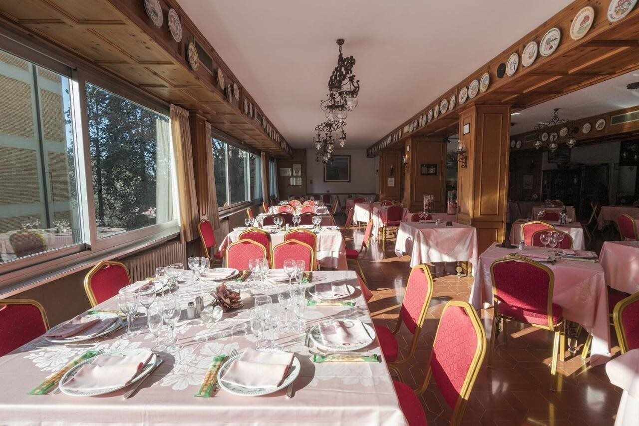 Zona pranzo con diversi tavoli apparecchiati, ampie finestre e un lampadario.