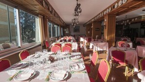 Un comedor con varias mesas listas para el servicio, ventanas amplias y una araña.