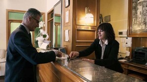 Zona de recepción de un hotel con mostrador de recepción, un reloj y cuadros en la pared.