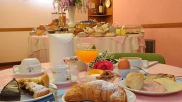 A breakfast buffet with various food items, a vase of flowers, and a clock on the wall.
