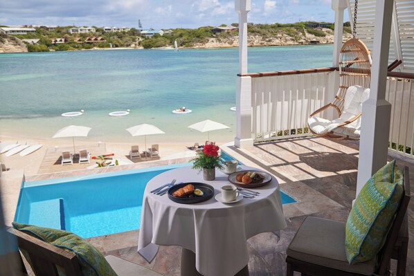 Mesa junto a la piscina con comida, una silla colgante y vista al mar.