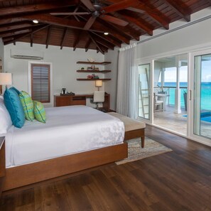 A bedroom with a large bed, wooden ceiling beams, a desk, and a view of the ocean through a sliding glass door. - Hammock Cove Resort And Spa (Willikies)