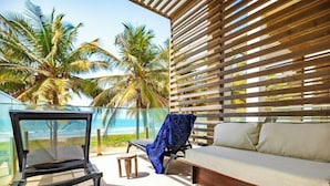 Un espace extérieur lumineux, aménagé avec un canapé et des fauteuils confortables, offrant une vue sur les palmiers et l’océan.