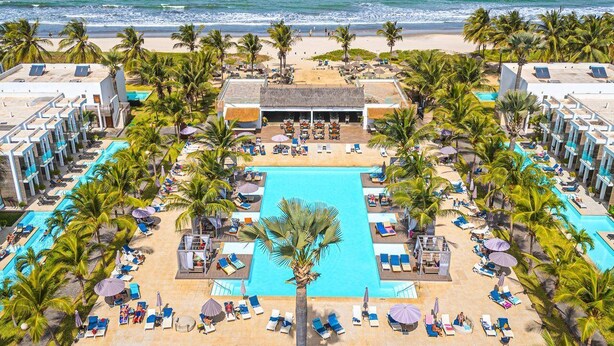 Un complexe hôtelier doté d’une piscine centrale, de chaises longues et de palmiers.