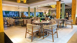 Un restaurant spacieux avec des tables rondes, des chaises en osier et des ventilateurs de plafond.