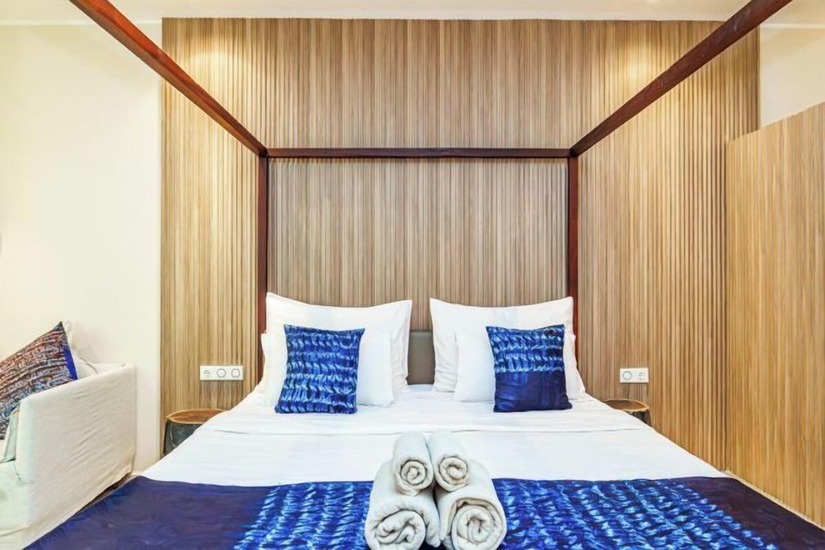 Quarto de hotel com uma cama grande, duas almofadas, cabeceira e mesa de cabeceira.