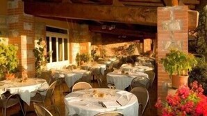 Un comedor interior con mesas redondas cubiertas con manteles blancos, paredes de ladrillo y plantas en macetas.