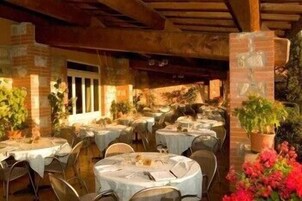 Un comedor interior con mesas redondas cubiertas con manteles blancos, paredes de ladrillo y plantas en macetas.