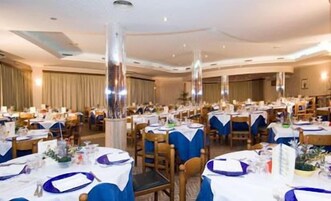 Un salón de banquetes con mesas redondas cubiertas con manteles blancos y fundas de sillas azules, dispuestas en filas.