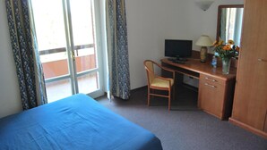 Habitación de hotel con cama, escritorio con computadora, silla, armario y ventana con cortinas.