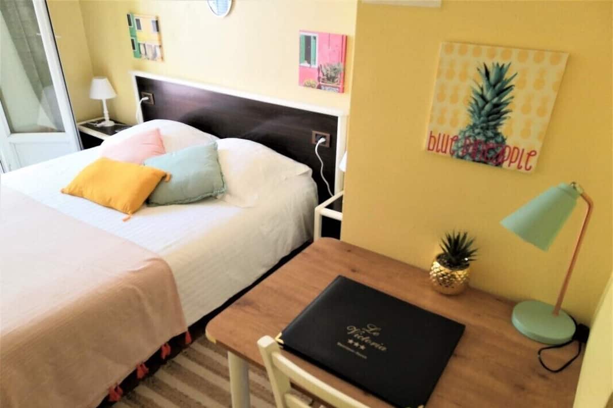 Una habitación de hotel con una cama, un escritorio, una silla, una lámpara, una piña y un cuadro con una piña en la pared.
