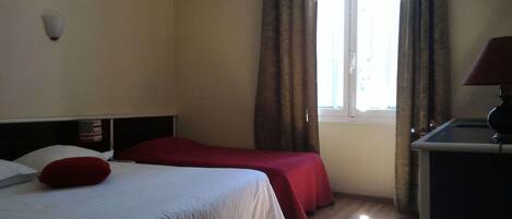 A hotel room with a bed, a desk, a lamp, a window with curtains, and a wall-mounted light.