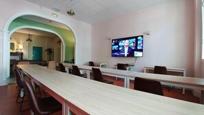 Une salle de conférence avec une longue table, des chaises, un écran de télévision et une arche donnant accès à une autre pièce.