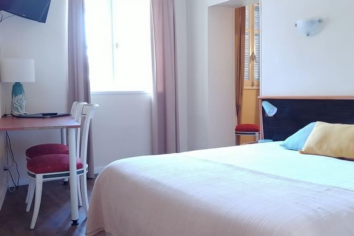 A hotel room with a bed, a desk with a chair, a television, and a window.