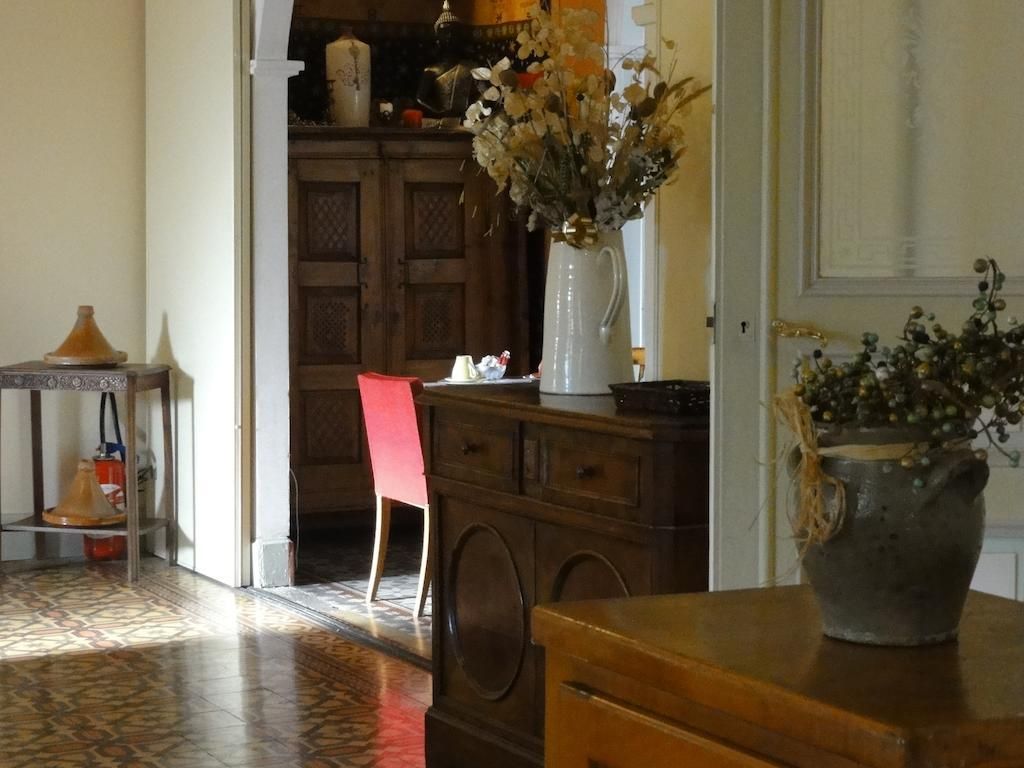 A room with a wooden cabinet, a red chair, a white vase with flowers, and a tiled floor.