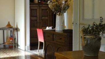 A room with a wooden cabinet, a red chair, a white vase with flowers, and a tiled floor.