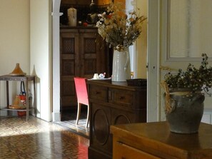 A room with a wooden cabinet, a red chair, a white vase with flowers, and a tiled floor. - Le Victoria (Draguignan)