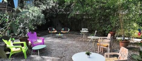Un espace patio aménagé avec des sièges d’extérieur, comprenant des chaises et des tables, entouré d’une végétation luxuriante et de plantes en pot.