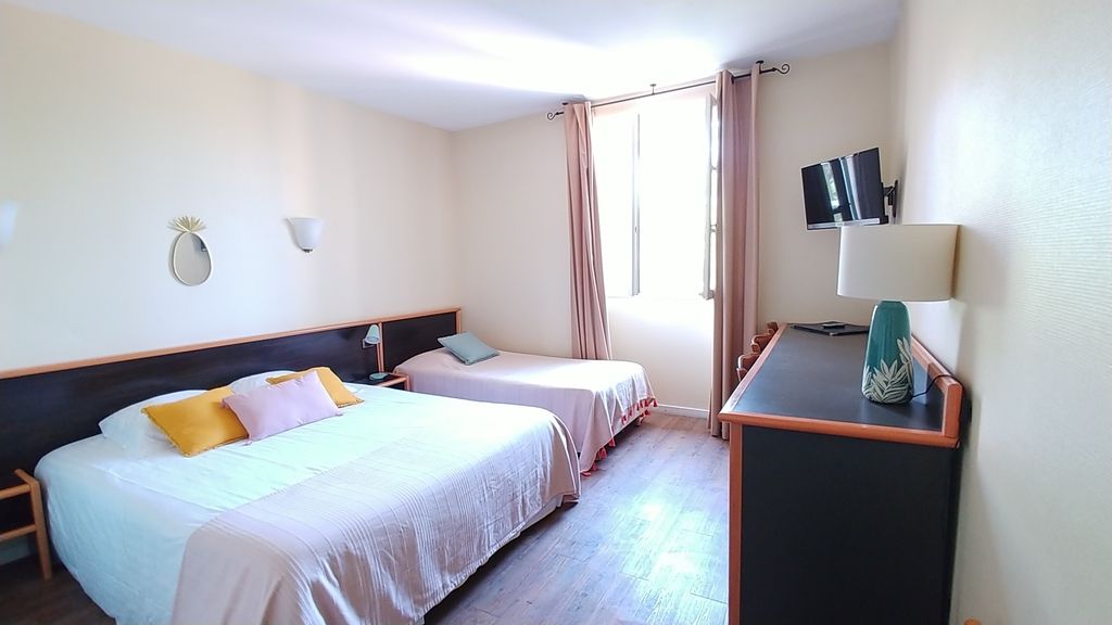 A hotel room with two beds, a desk, a TV, and a window with curtains.
