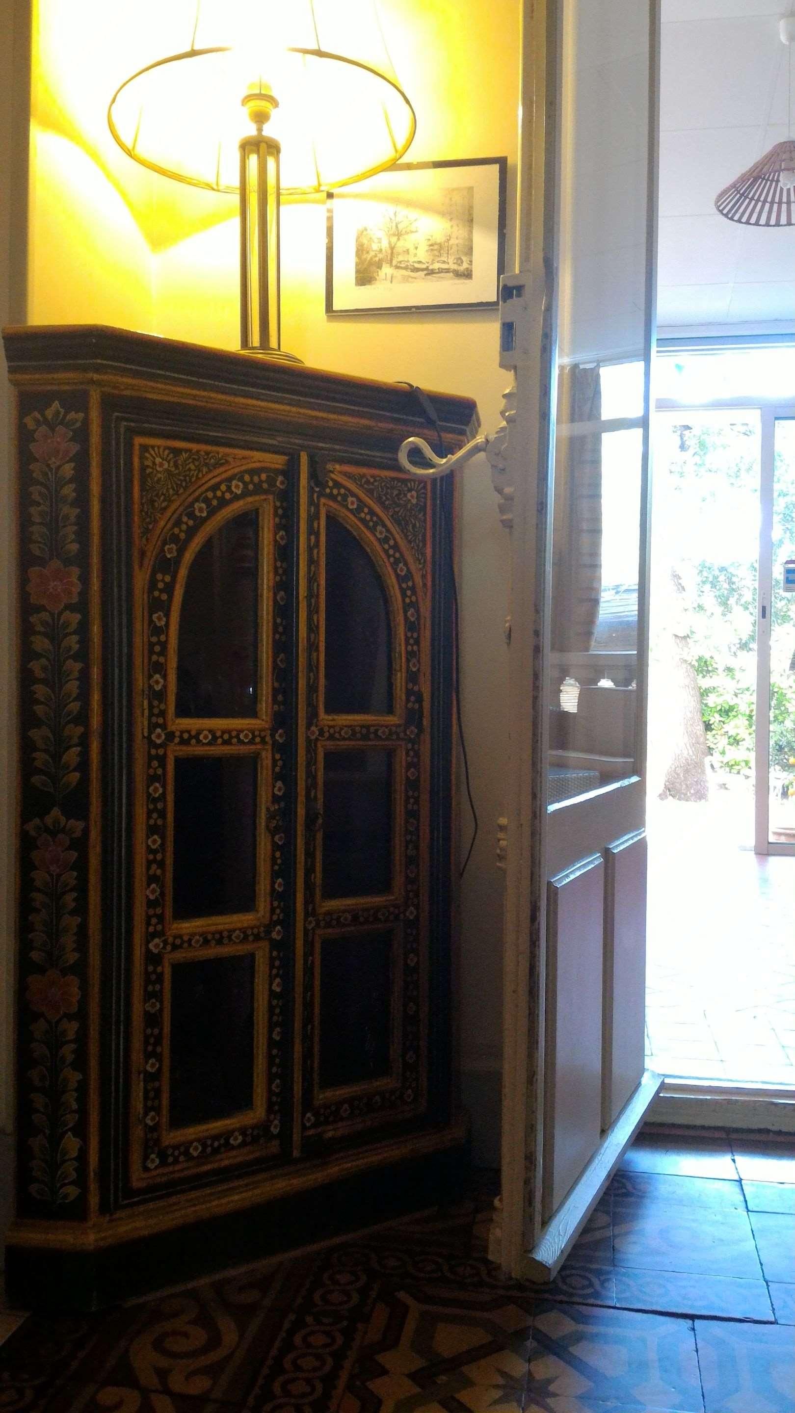 Una habitación con piso estampado, un mueble decorativo, una lámpara y un cuadro en la pared.