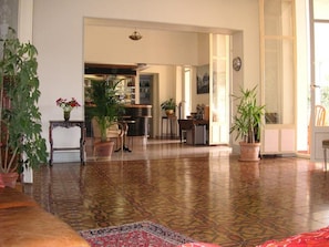 A spacious living area with a patterned floor, potted plants, and a view into the kitchen. - Le Victoria (Draguignan)