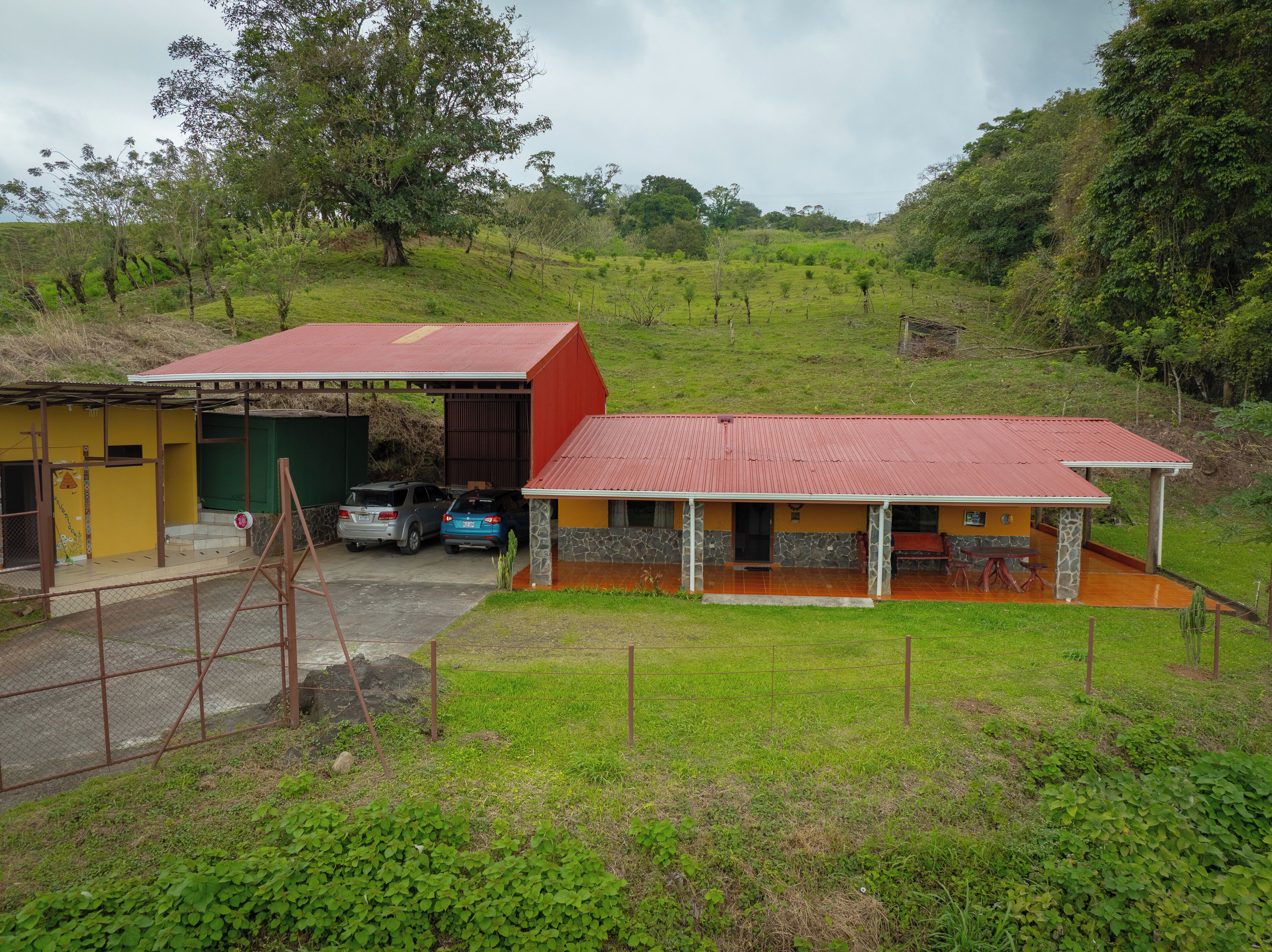 A rural property with a large red barn, a yellow building with a covered porch, and two parked cars.