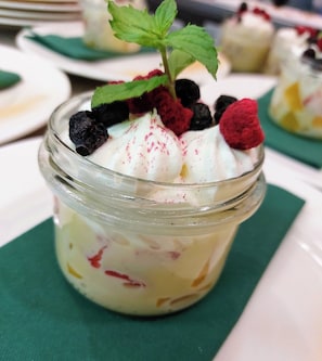 A dessert in a glass jar with whipped cream, berries, and a mint leaf on top. - Queens Apartments (Kraków)