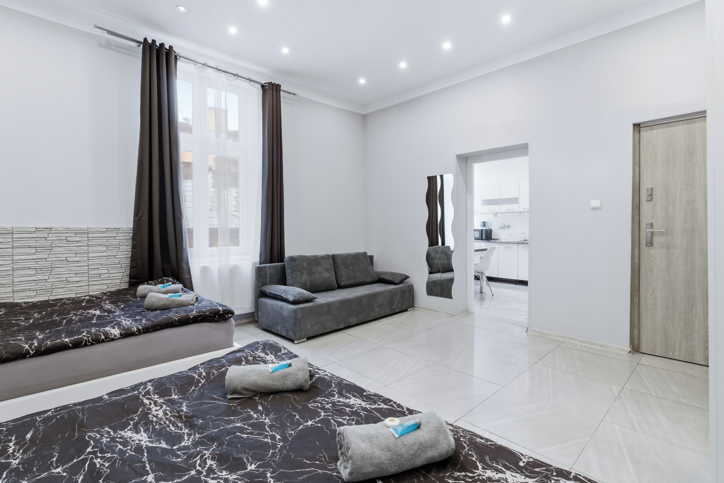 A modern hotel room with a bed, sofa, and a view of the city.