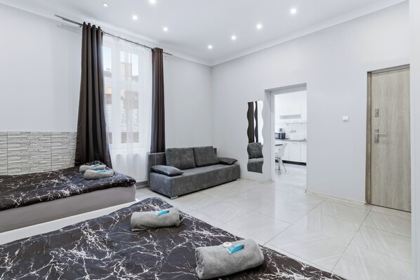 A modern hotel room with a bed, sofa, and a view of the city. - Queens Apartments (Kraków)